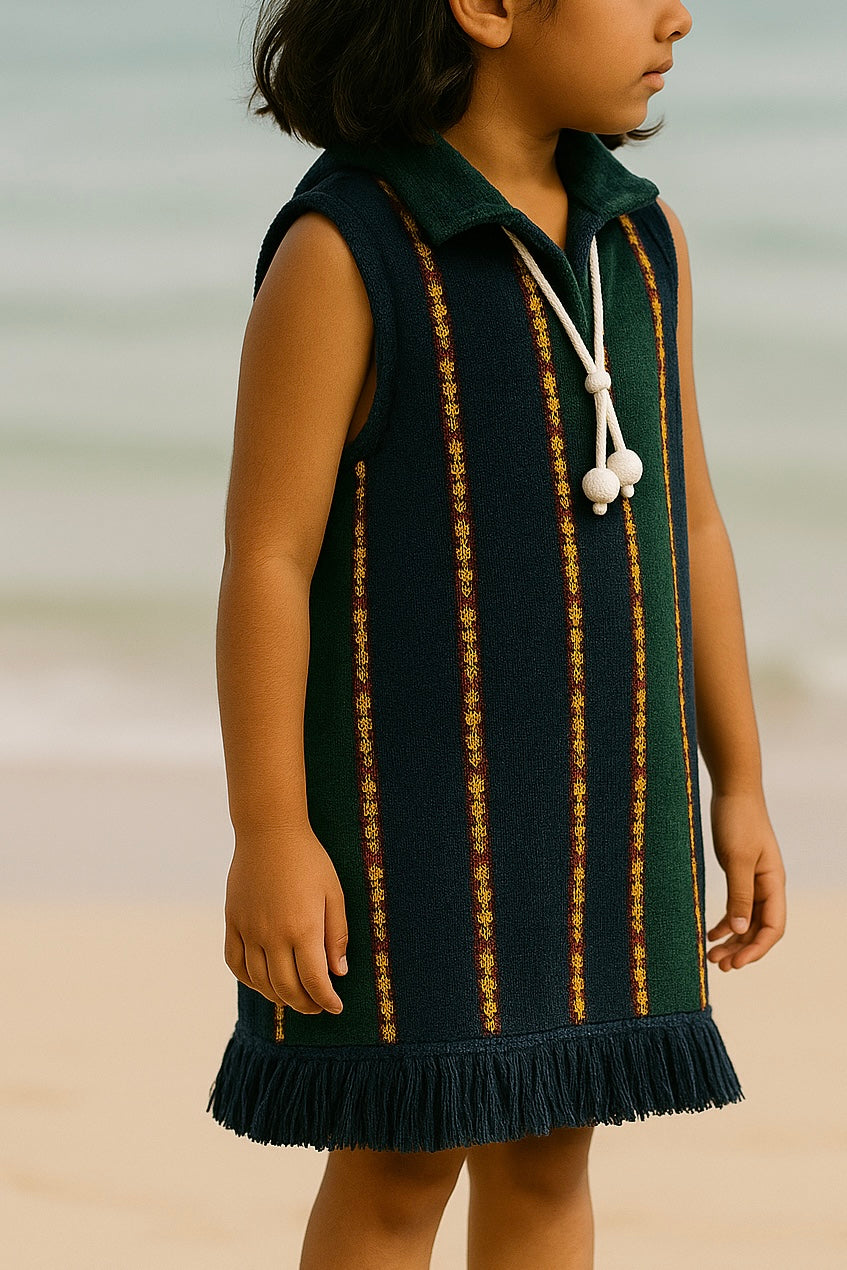Young girl wearing a green dress with gold stripes on a beach.