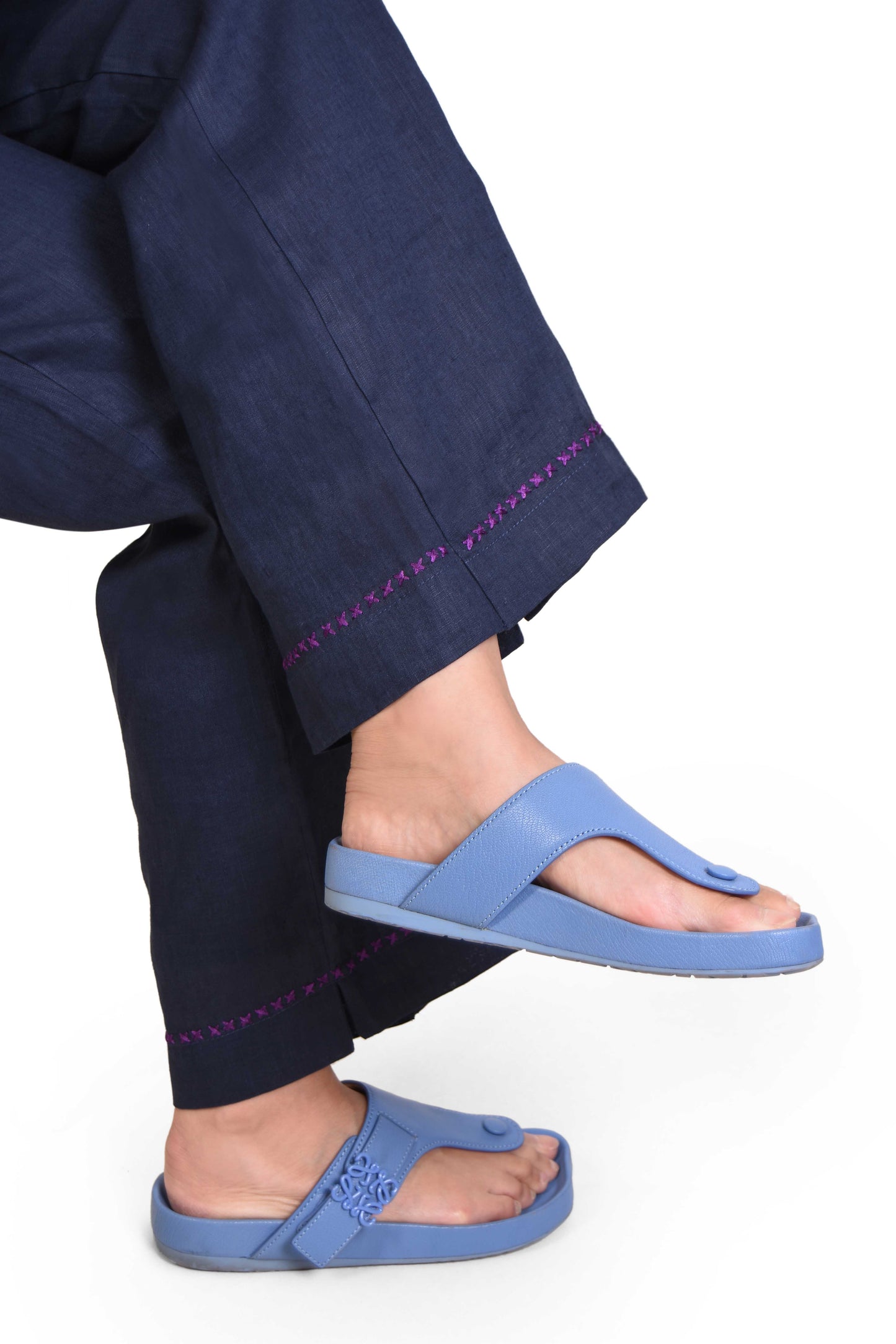 Person wearing blue sandals with navy pants, Indian Linen, on a white background