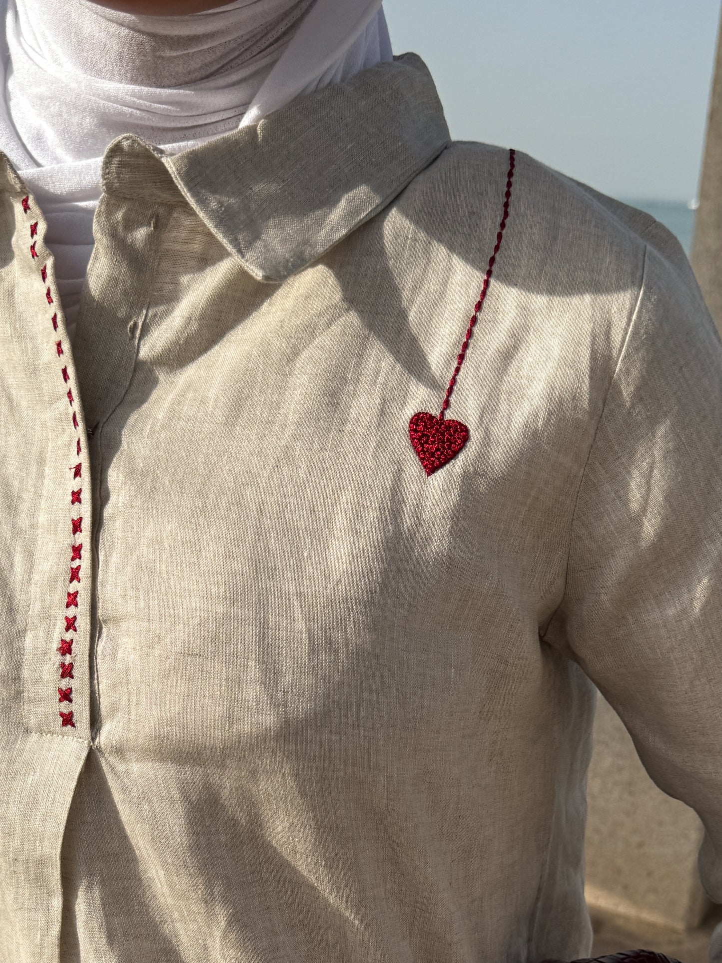 Close-up of a beige shirt with a red heart design and white scarf, blurred background