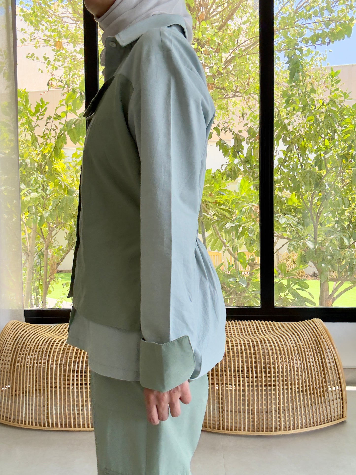Woman in a light green summer suit standing by a window with garden view. sustainable fashion look