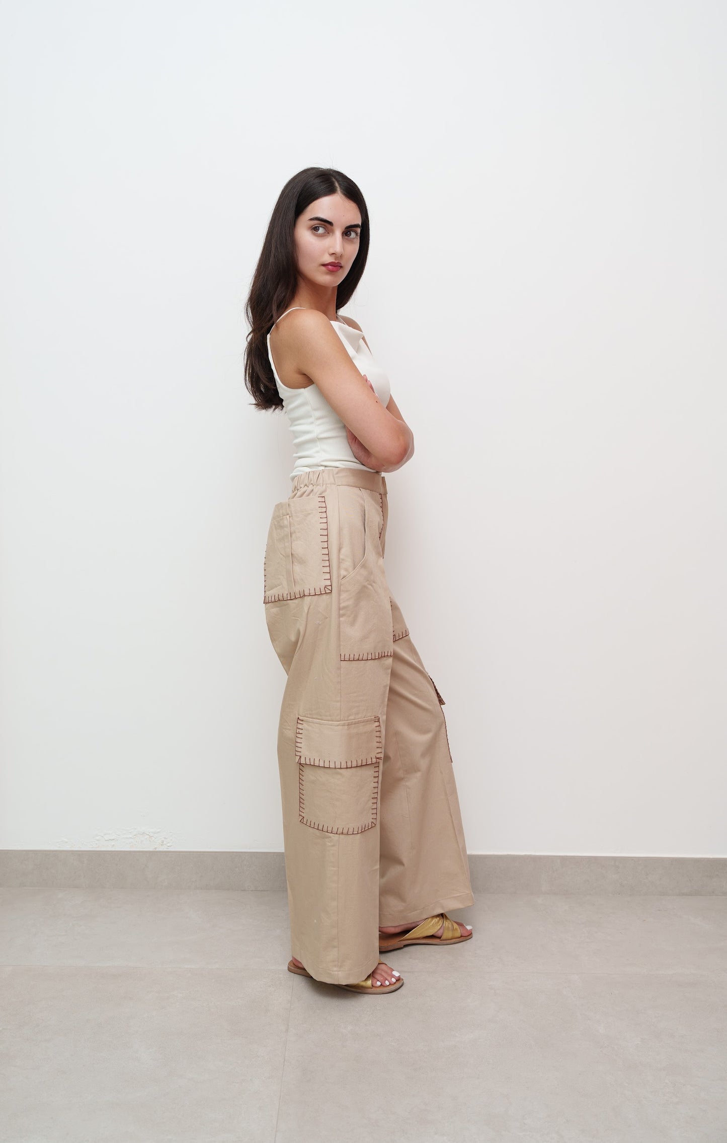 Woman wearing a white sleeveless top and beige cargo pants against a white background