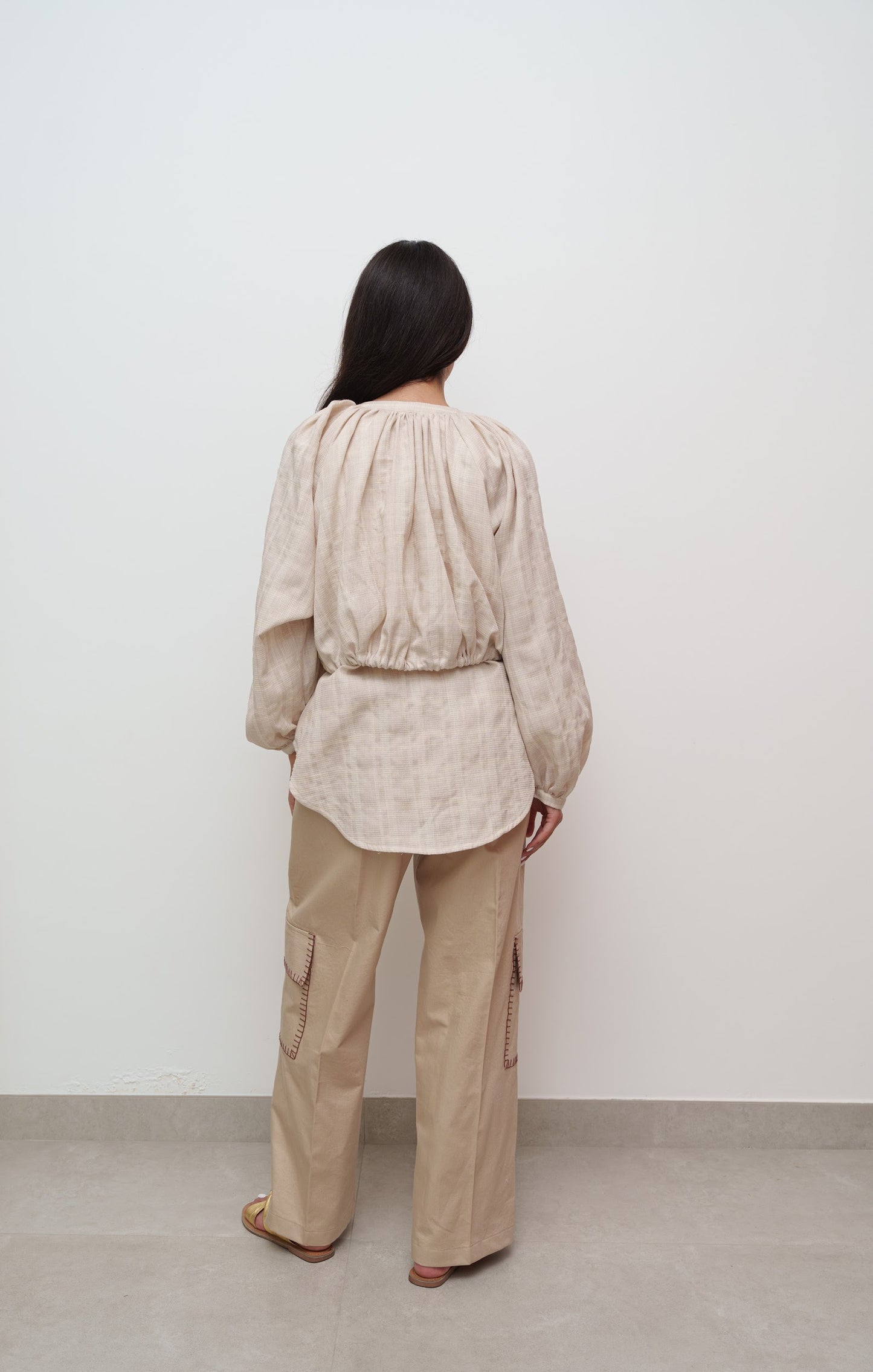 Person wearing a beige outfit with a shirt and cargo pants against a white wall.