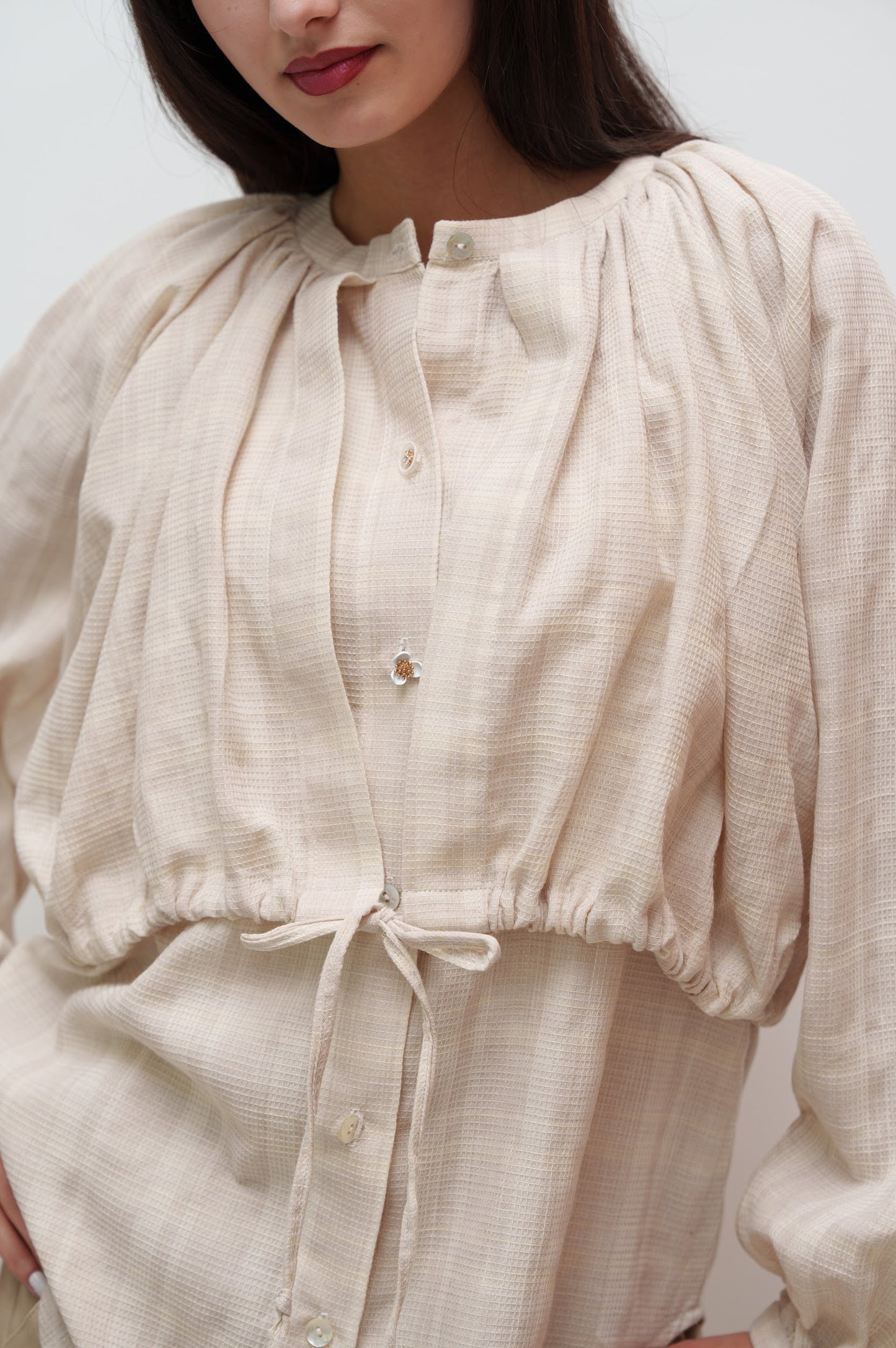 Woman wearing a beige blouse with puffed sleeves against a plain background