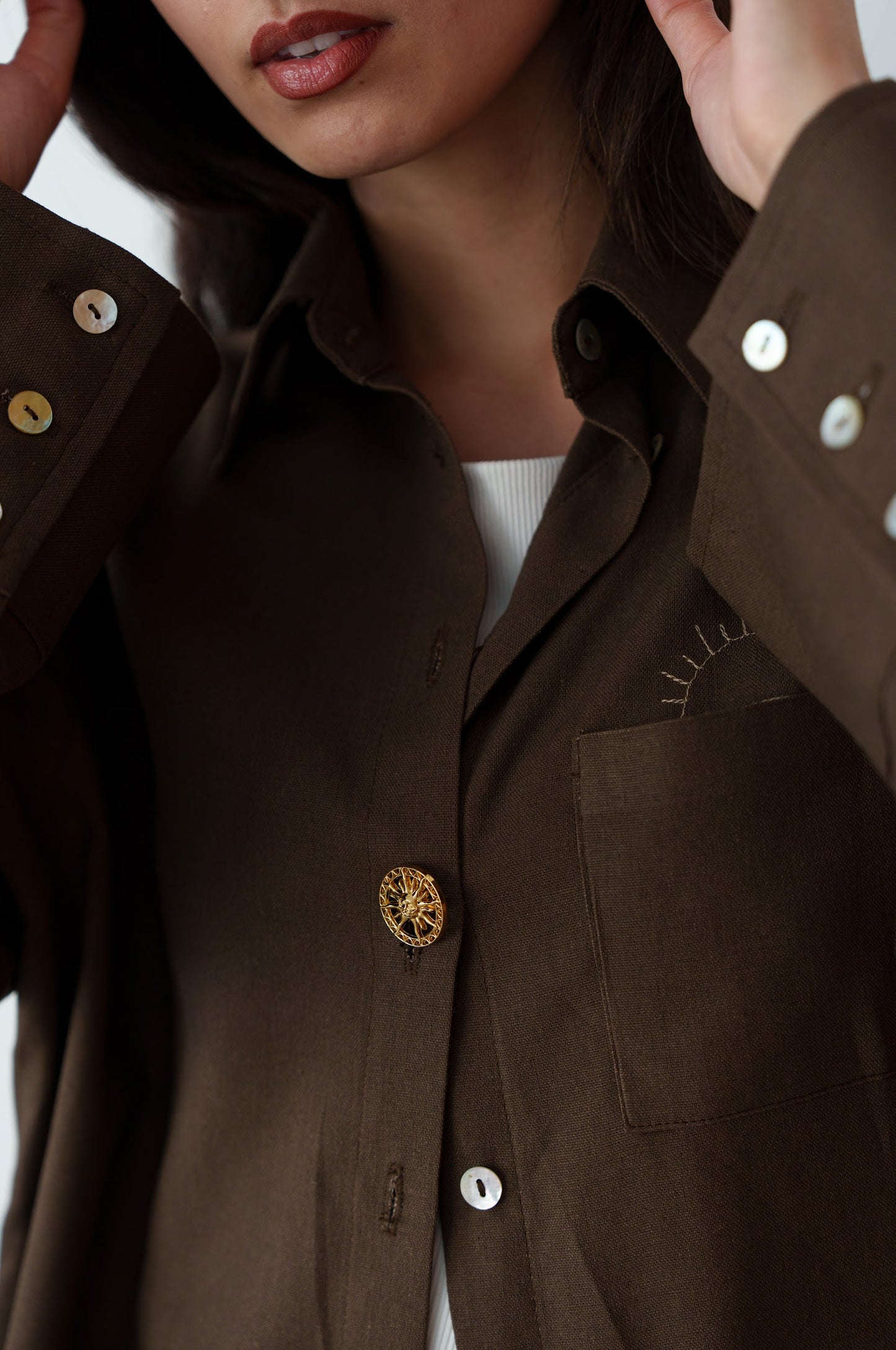 Close-up of person wearing a brown button-up shirt on a white background.