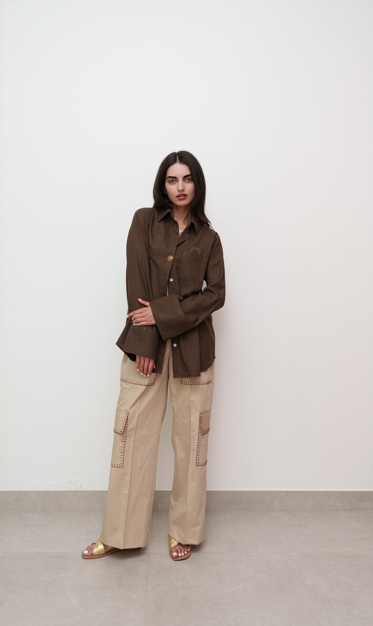 Woman wearing a brown jacket and beige pants against a white background