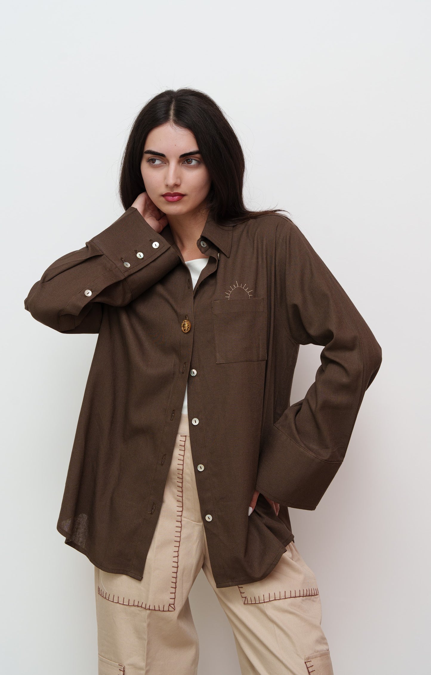 Woman wearing a brown jacket and beige pants against a white background
