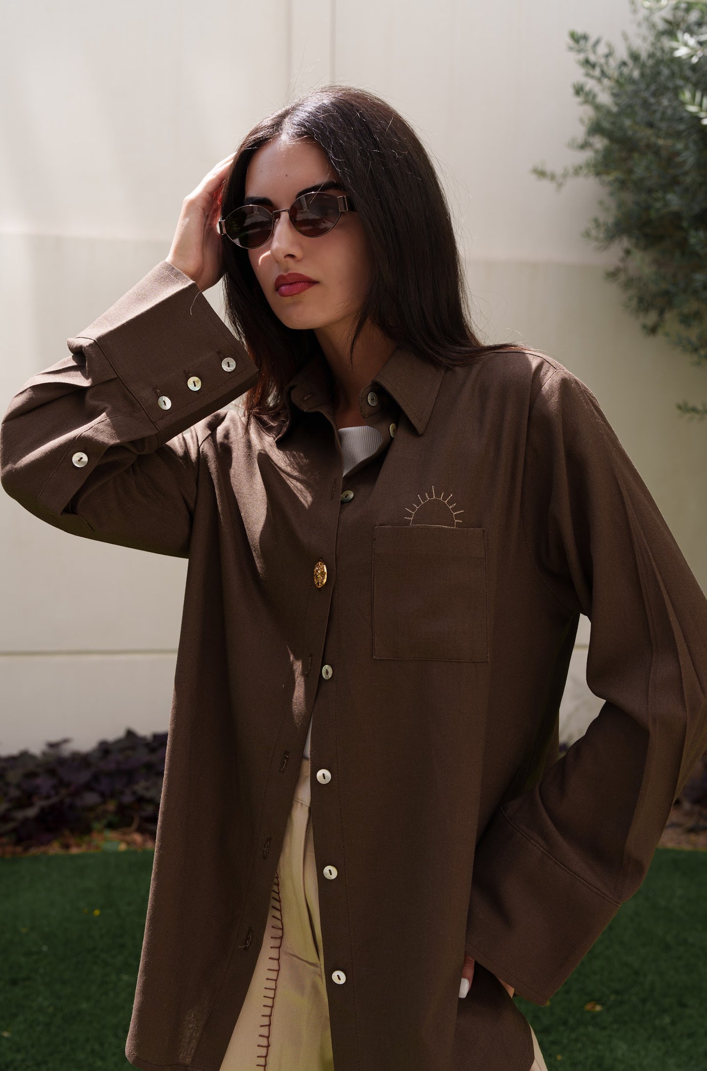 Woman wearing a brown shirt with a logo, standing outdoors.