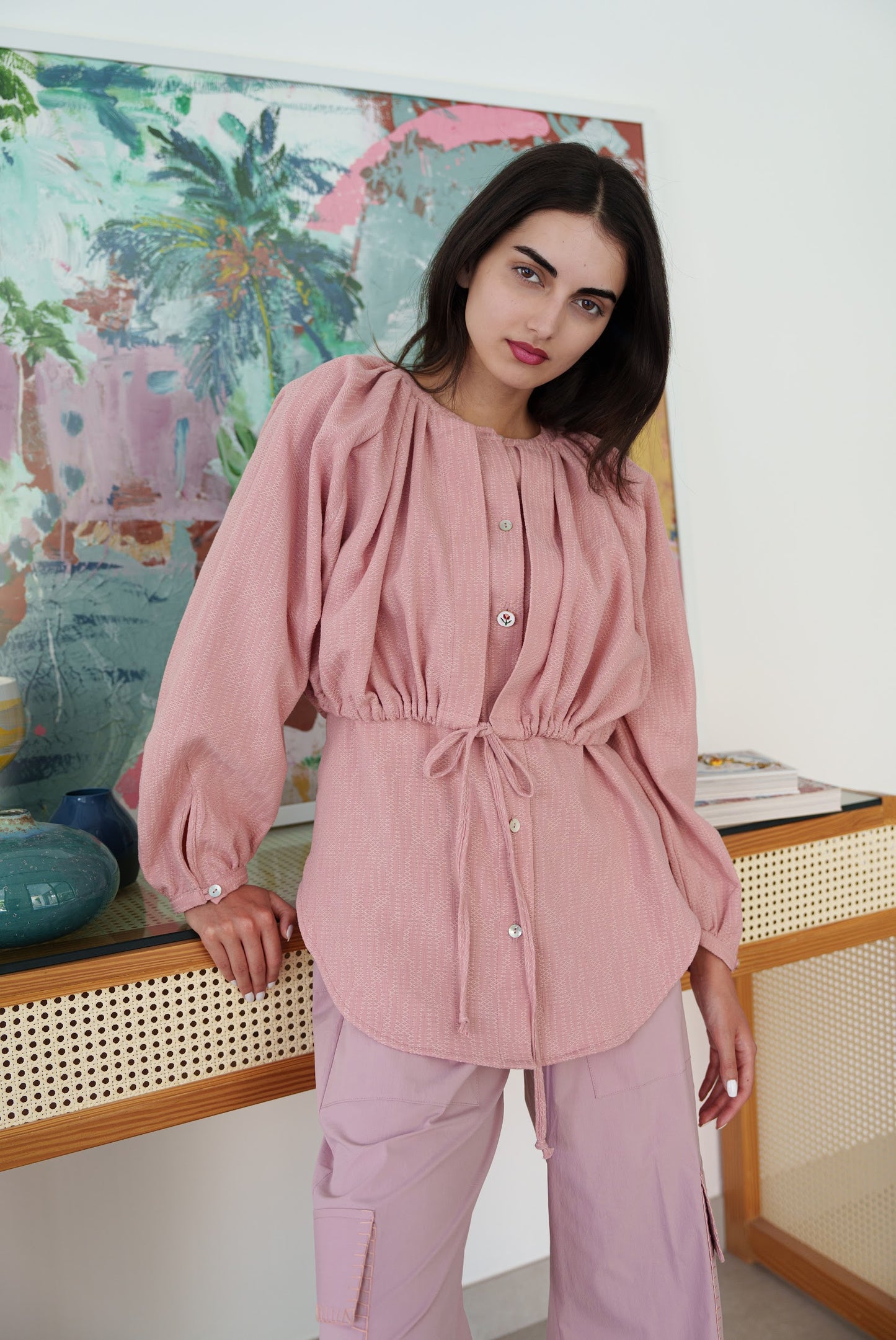 Woman wearing a pink top and pants in a room with a colorful abstract painting on the wall.