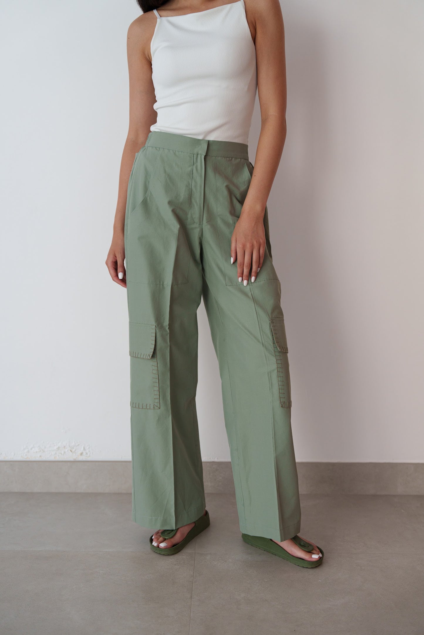 Person wearing green pants and a white top against a plain background
