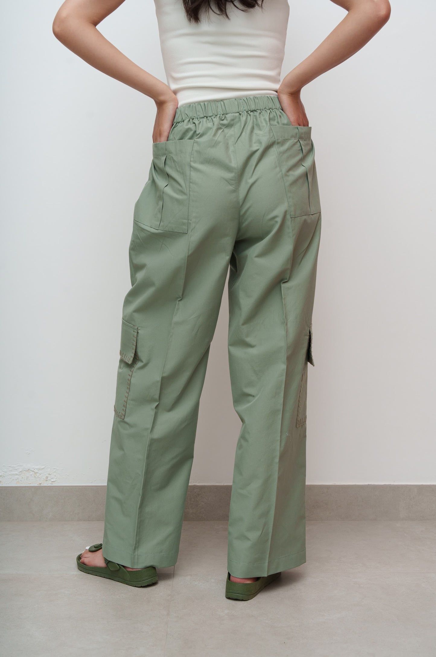 Person wearing green cargo pants and a white top against a plain background
