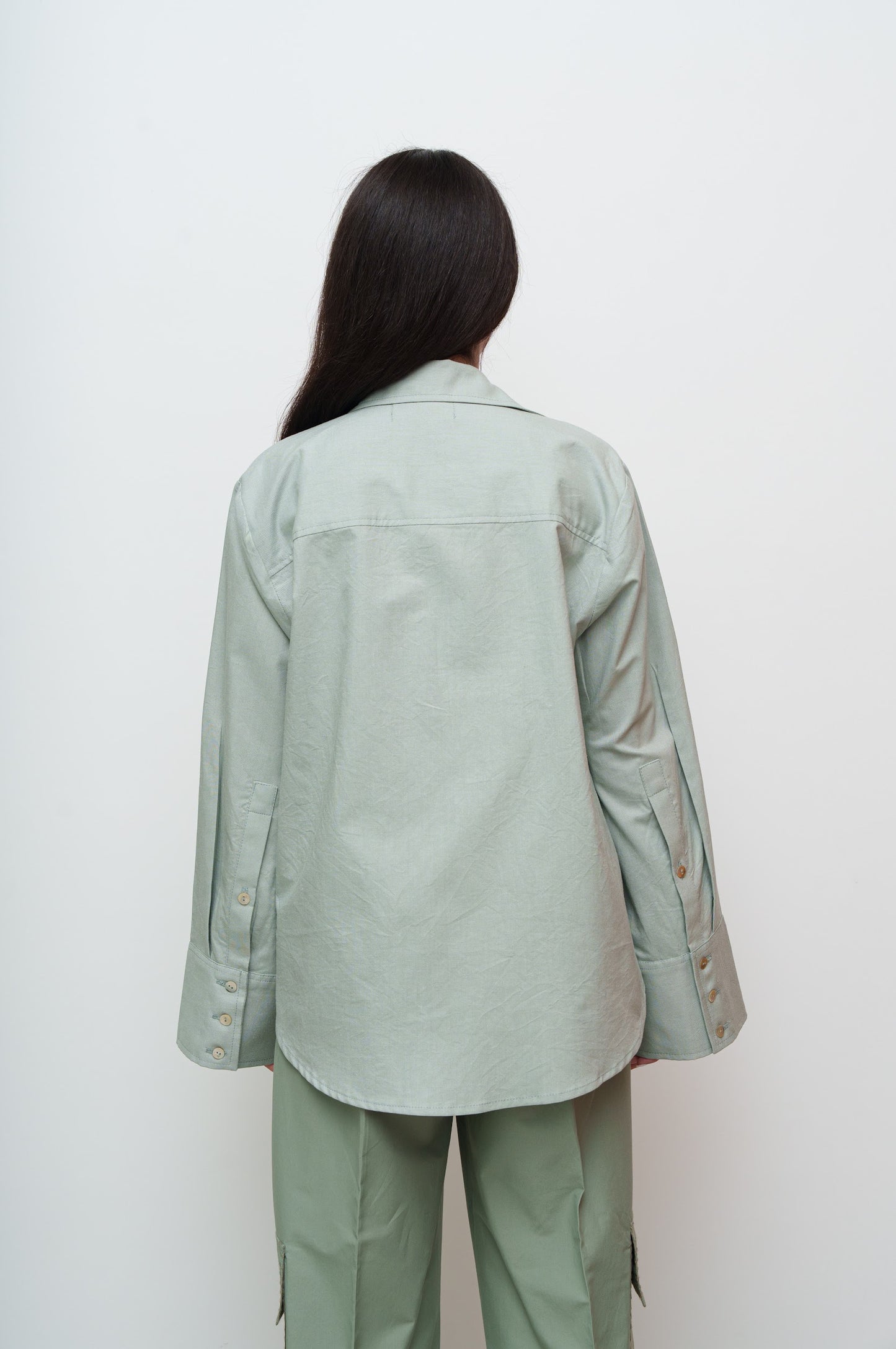 Person wearing a light green jacket and pants against a white background