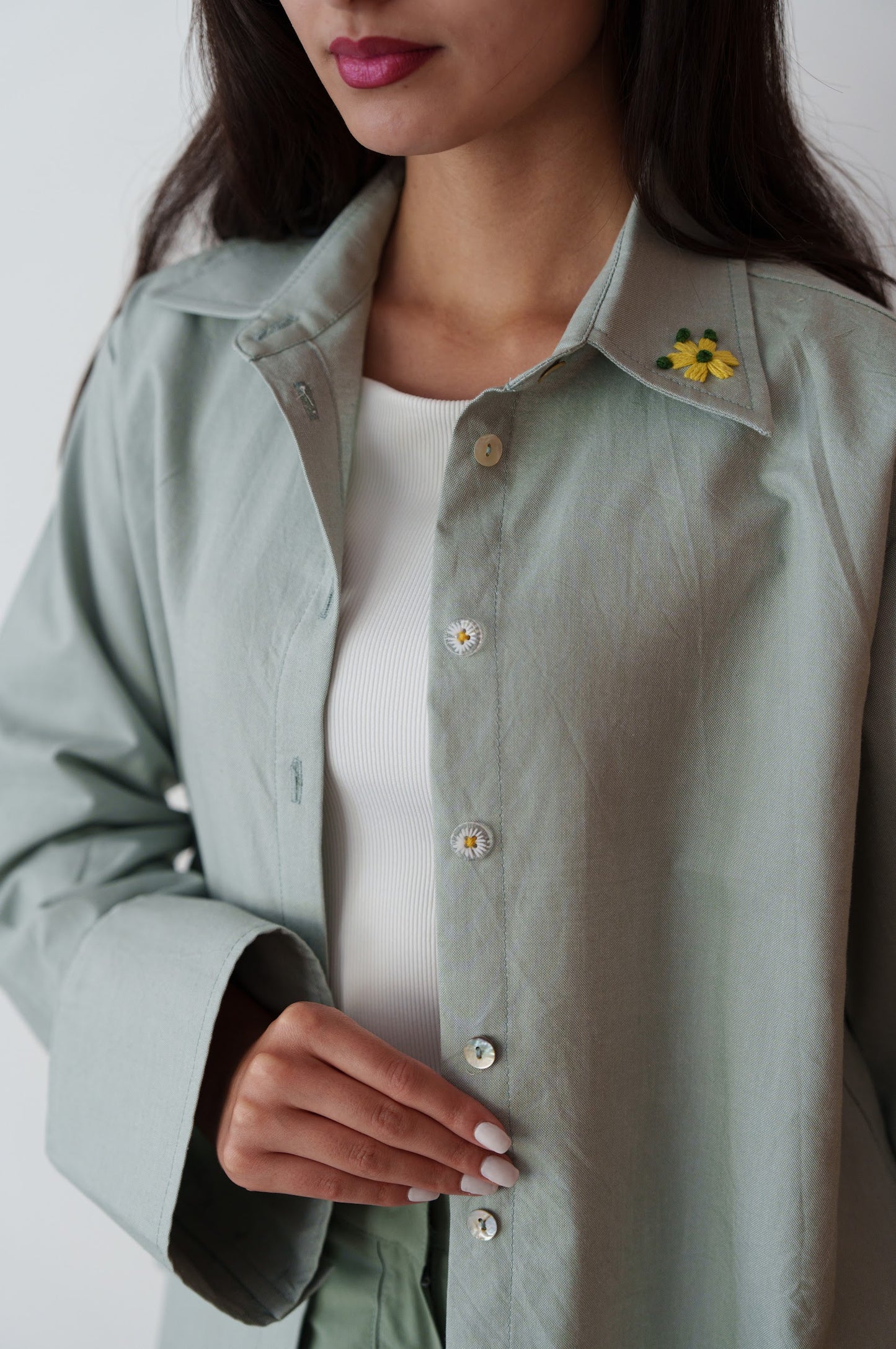 Person wearing a light green button-up shirt with a floral pin on a white background