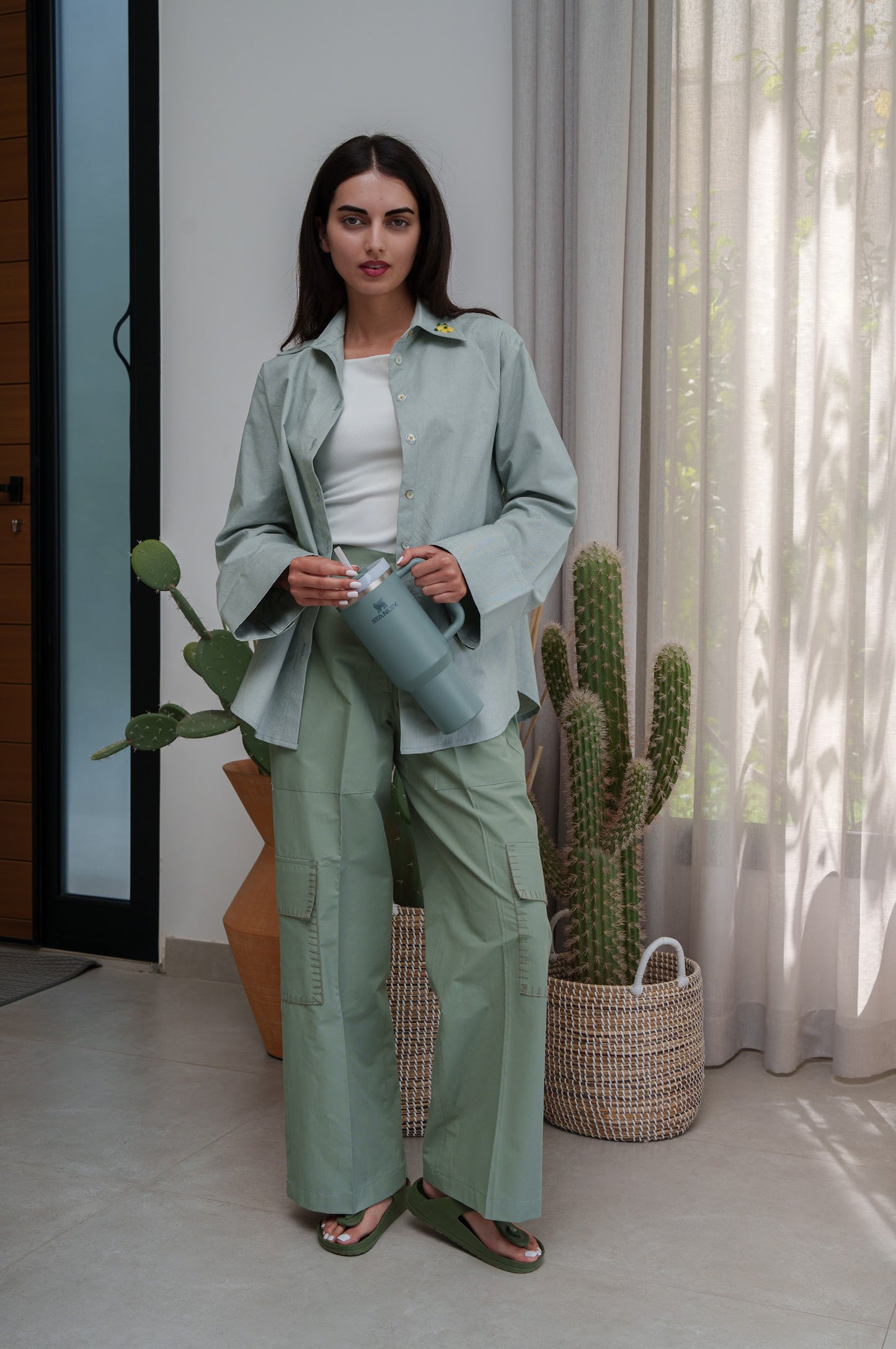 Woman in a green outfit holding a watering can in a room with cacti.