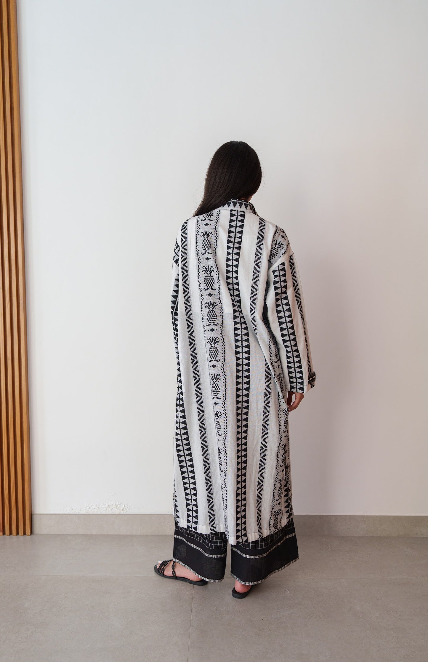 Woman wearing a long, patterned dress standing against a plain wall.