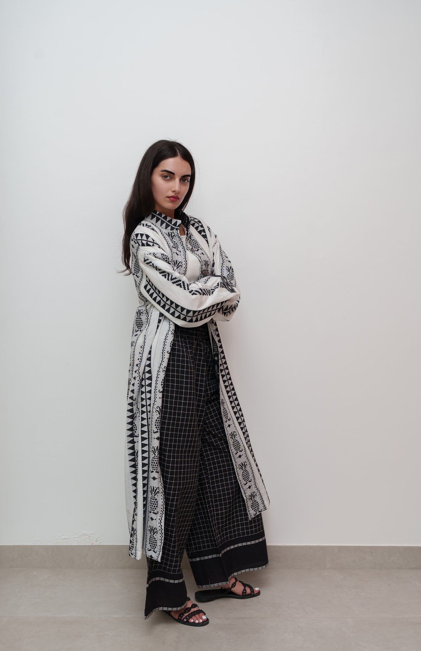 Woman wearing a long, patterned coat over a black and white checkered dress against a plain background.