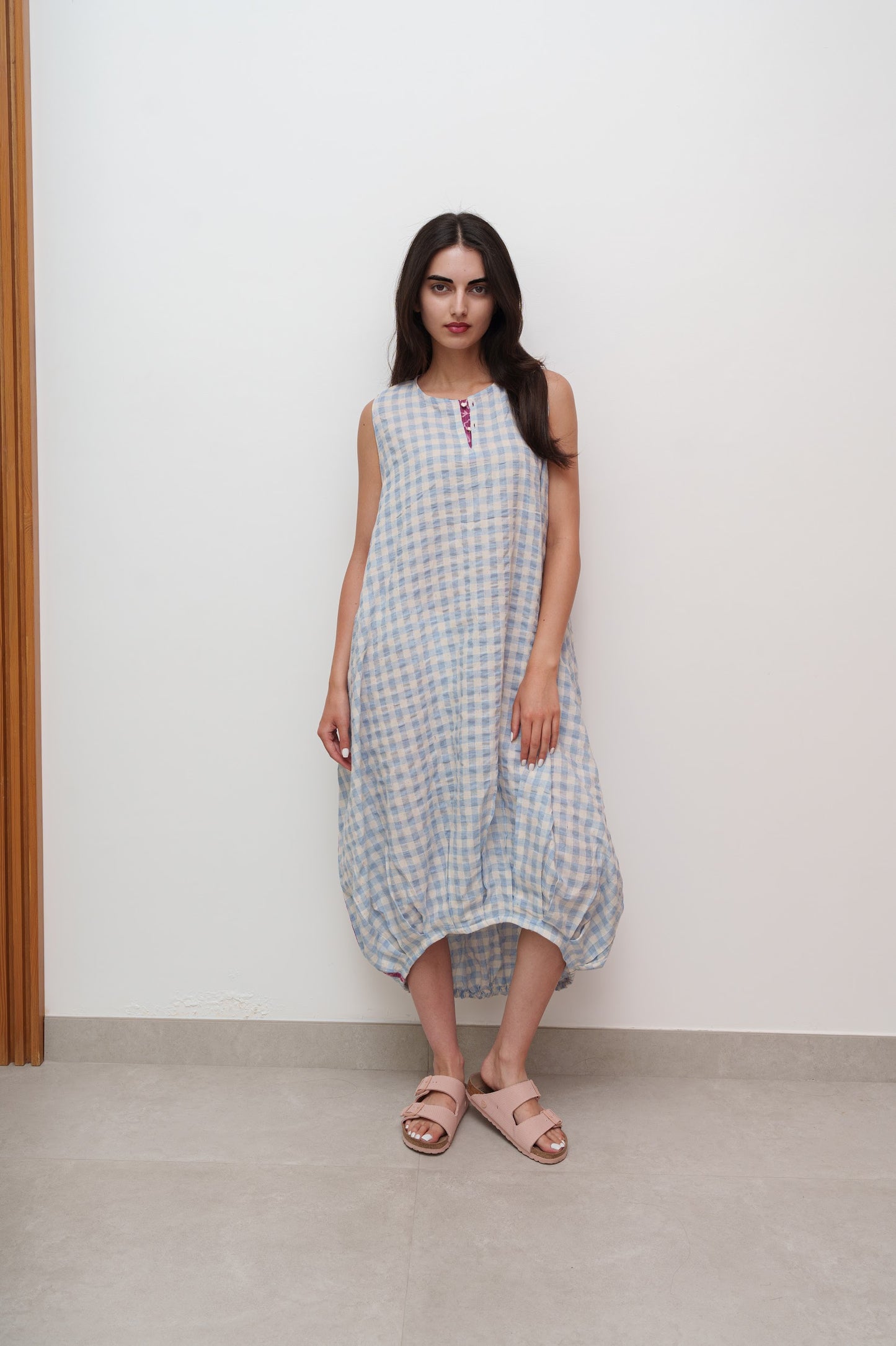 Woman wearing a checkered dress standing against a white wall.