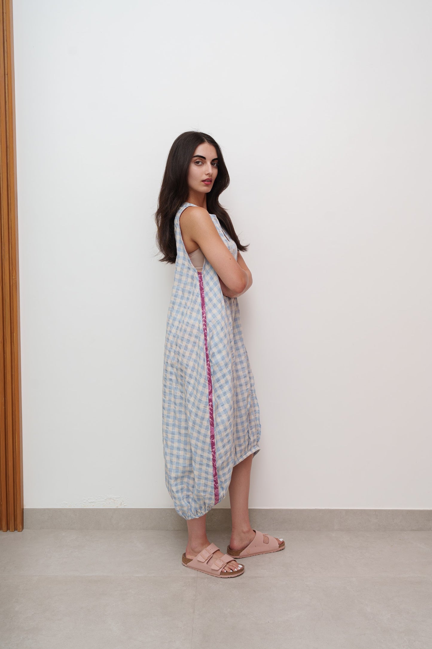 Woman wearing a checkered dress with a red border against a white wall.