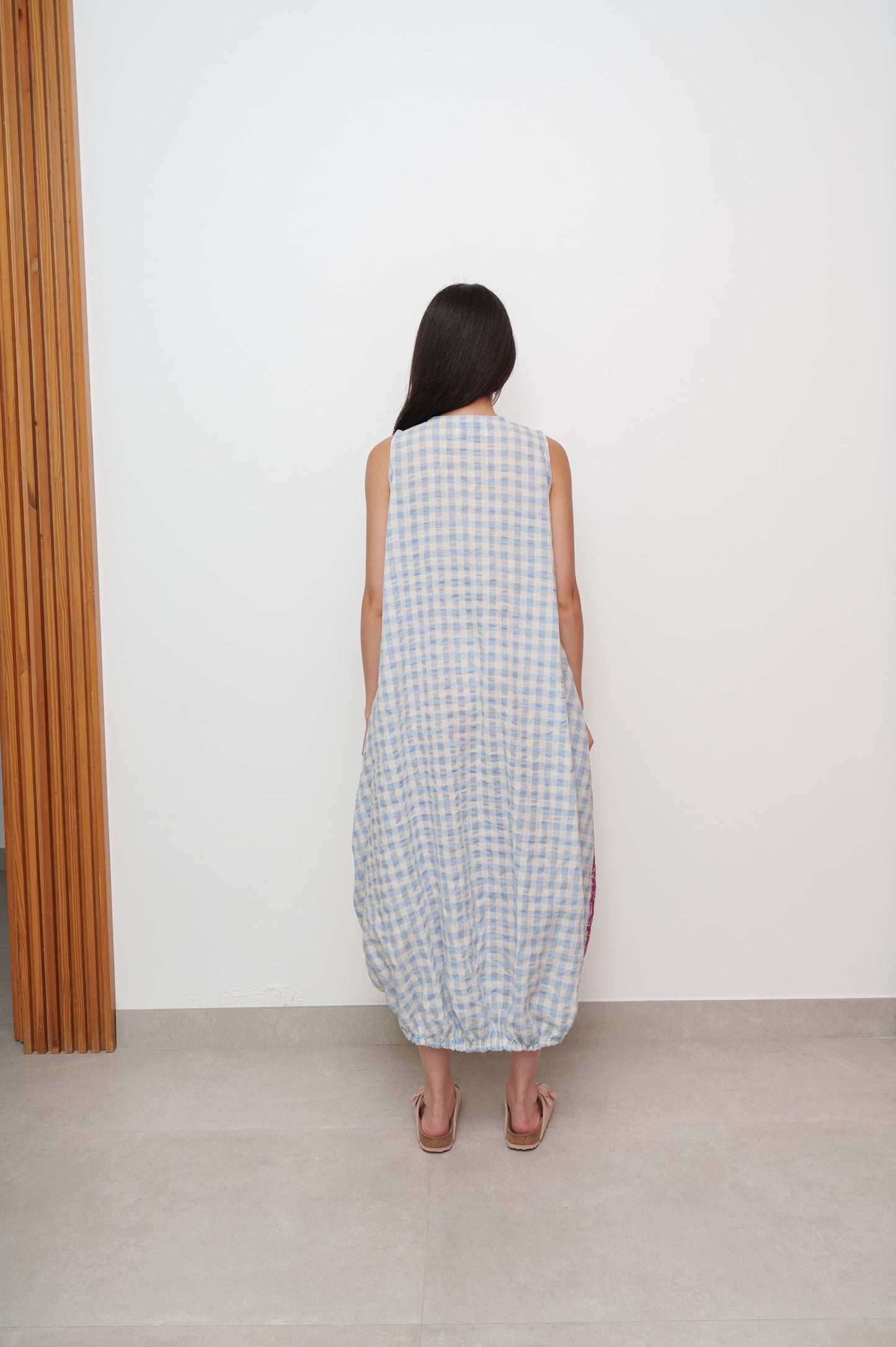 Backside of checkered dress with sleeveless design, worn by woman against plain white wall.