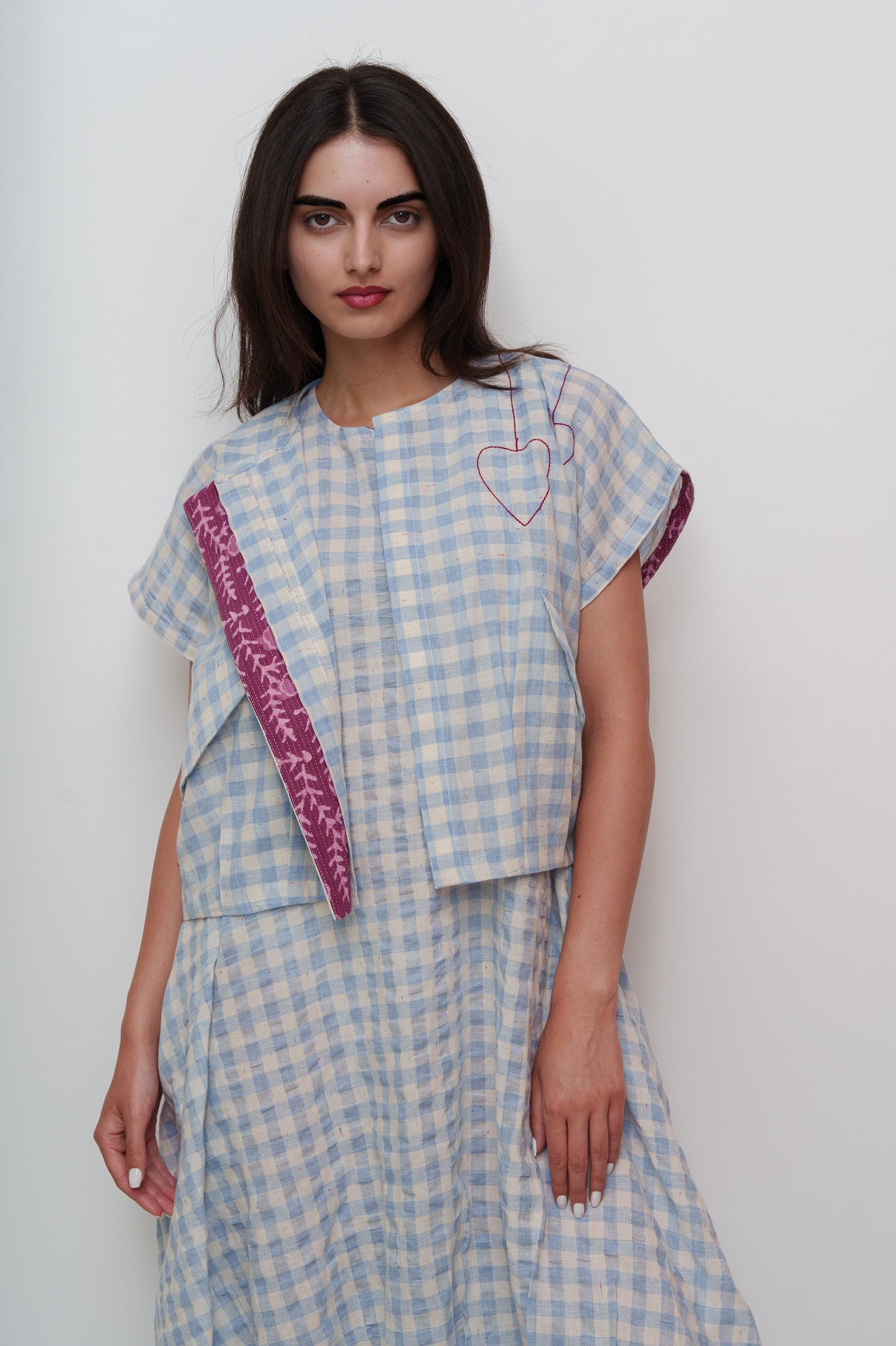 Woman wearing a blue checkered outfit with a pink strap over a white background