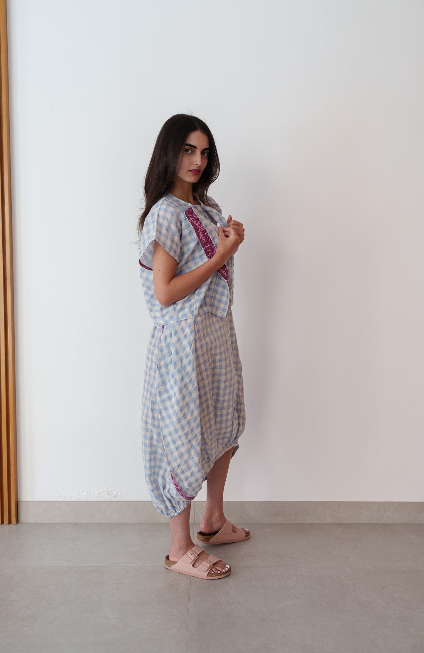 Woman wearing a light blue checkered dress with a pink stripe in a minimalistic setting.