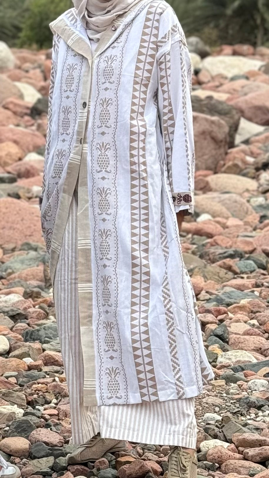 Person wearing a long, patterned dress standing on a rocky beach.