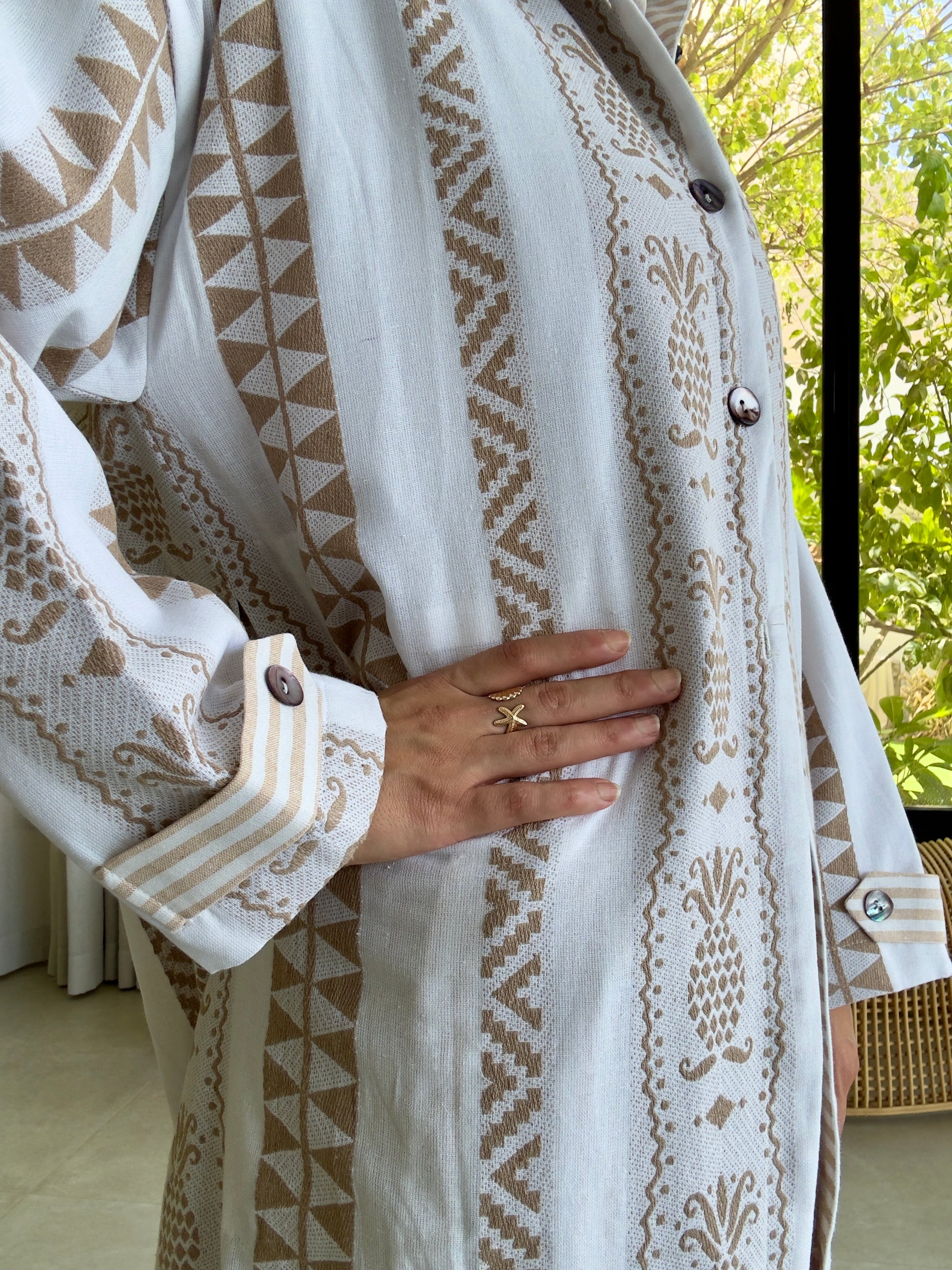 Close-up of hand-embroidered white top with brown geometric patterns and front buttons, artisanal fashion detail.