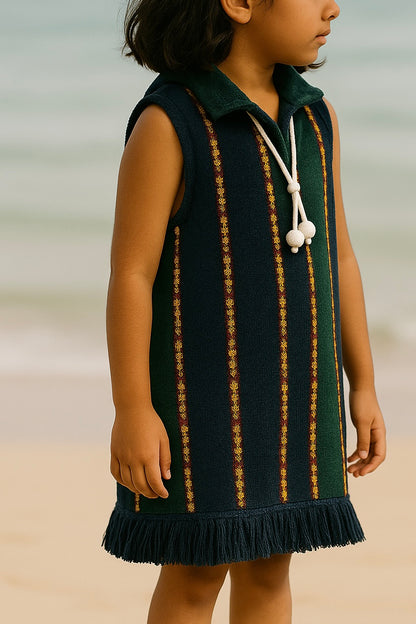 Young girl wearing a green dress with gold stripes on a beach.