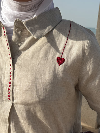 Close-up of a beige shirt with a red heart design and white scarf, blurred background