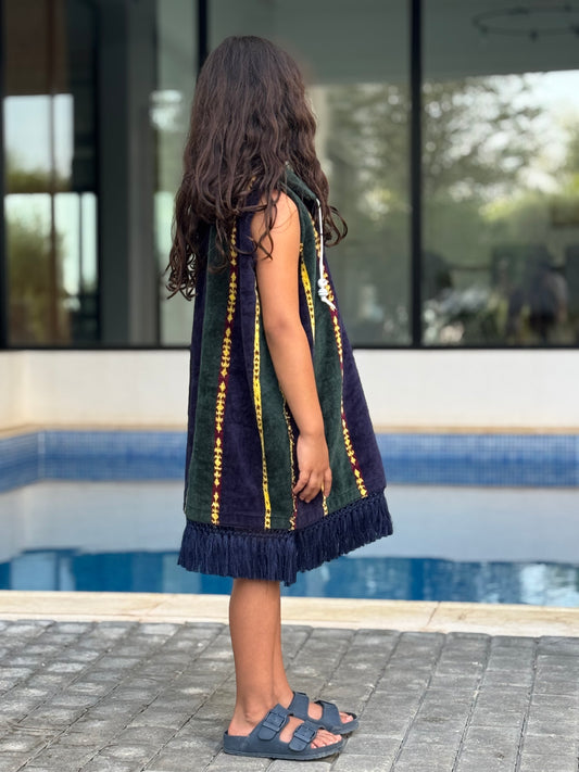 Child wearing a dark green and yellow dress with ruffles by a poolside.