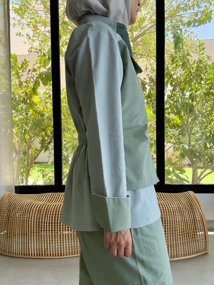 Person wearing a light green outfit standing in front of a window with a view of trees.