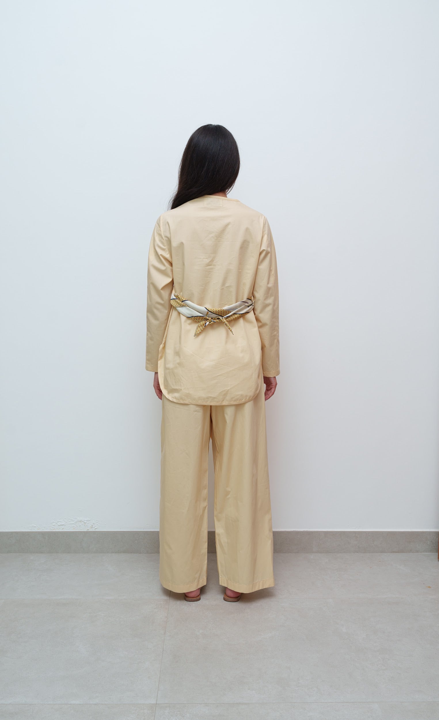 Person wearing a beige outfit with a belt against a white wall