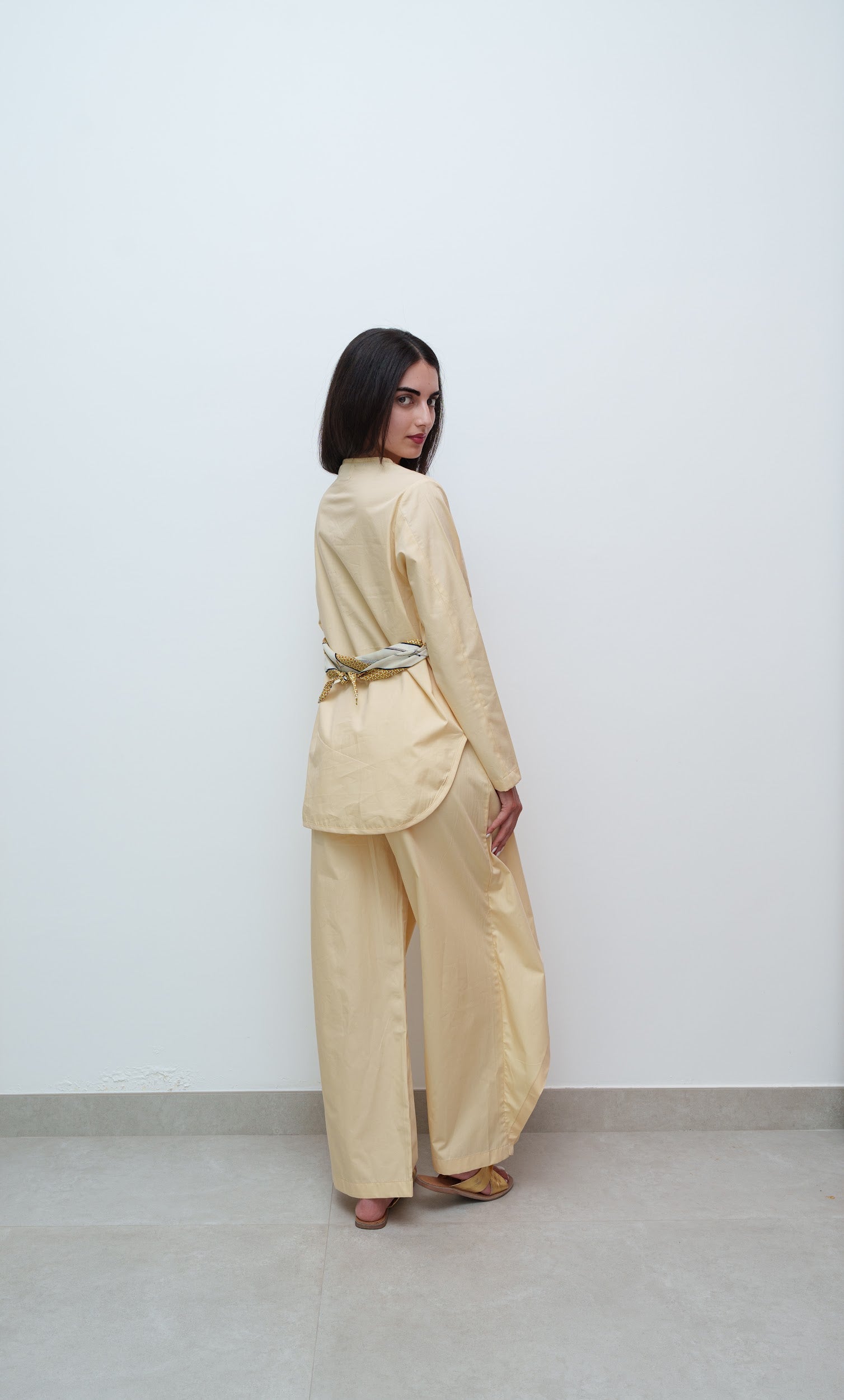 Woman wearing a beige outfit with a belt against a white background