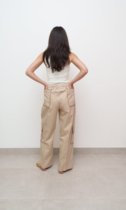 Person wearing beige cargo pants and a white top against a plain background