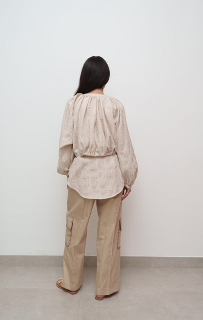 Person wearing a beige outfit with a shirt and cargo pants against a white wall.