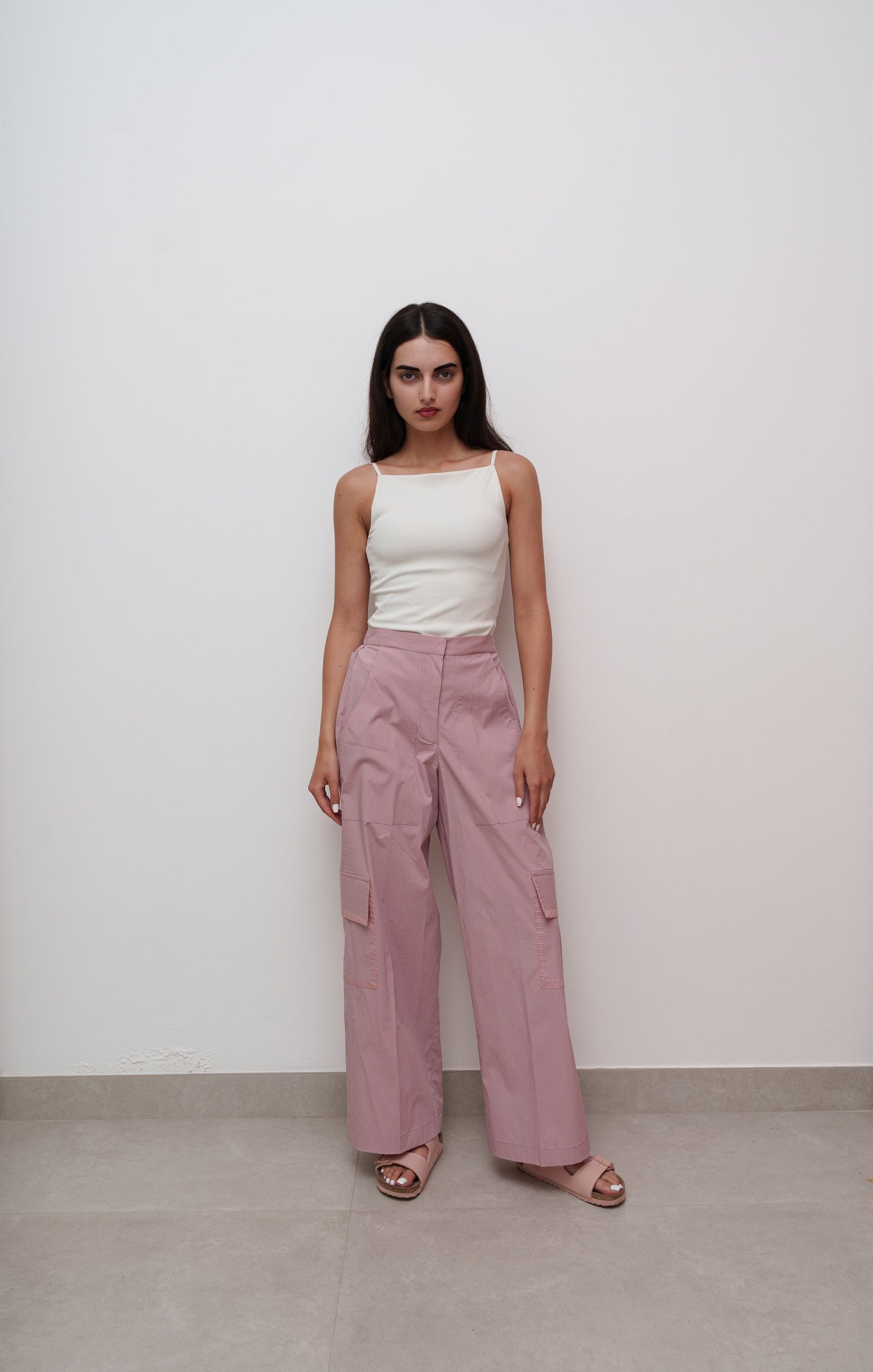 Woman wearing a white top and pink pants against a plain background