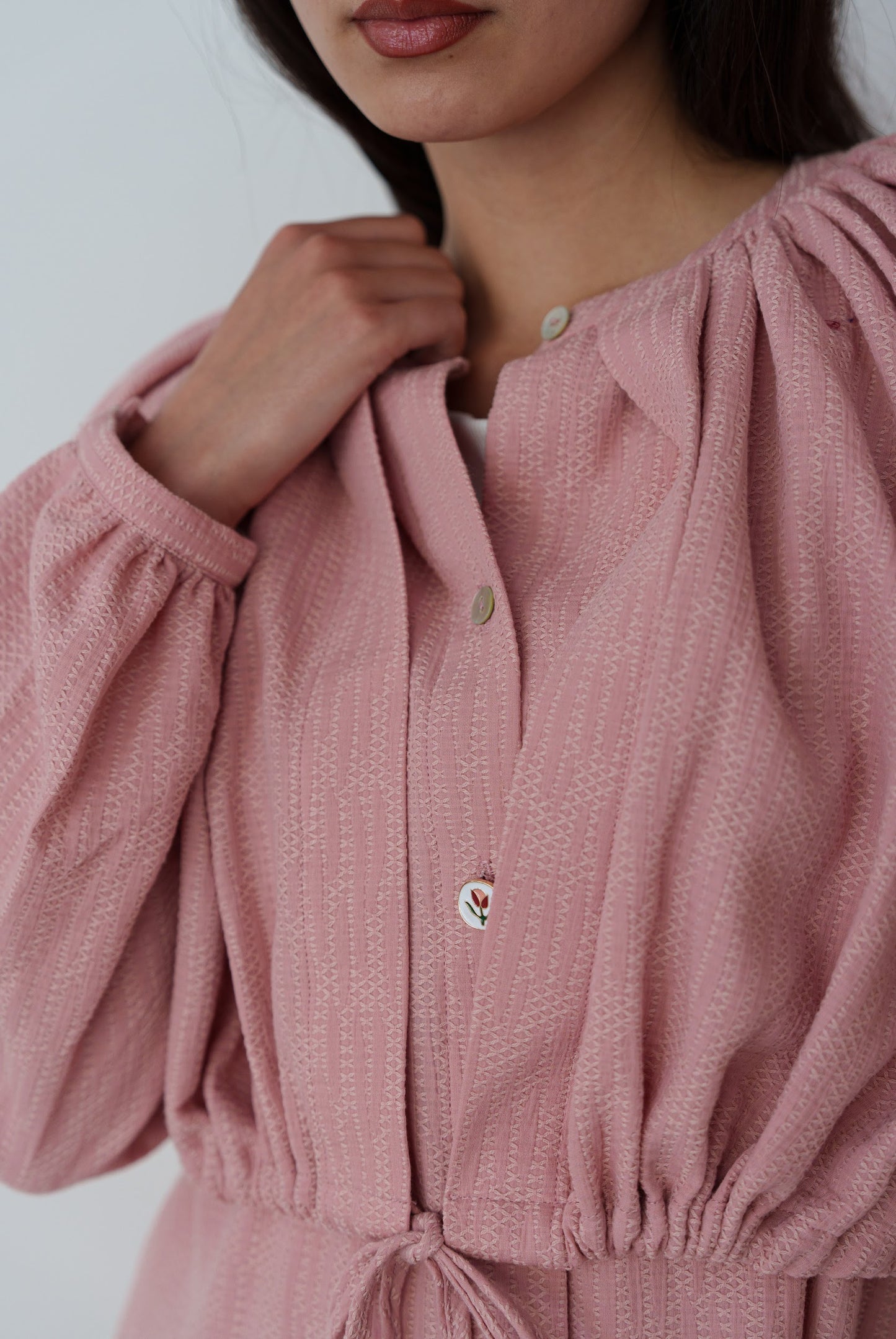 Close-up of a person wearing a pink textured dress with button details.