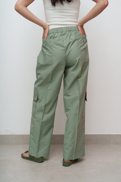 Person wearing green cargo pants and a white top against a plain background