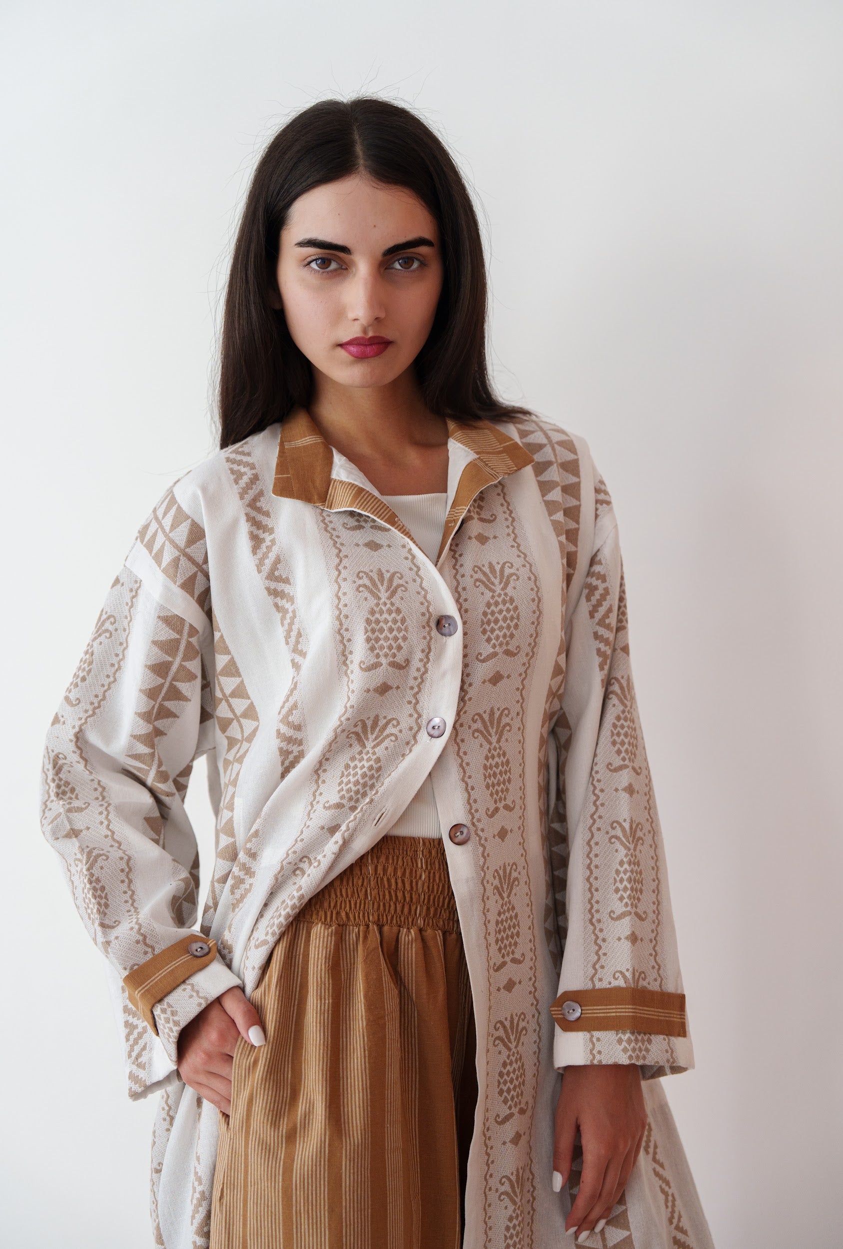 Woman wearing a patterned beige and white jacket over a brown dress against a white background
