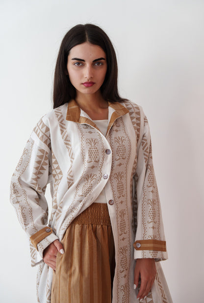 Woman wearing a patterned beige and white jacket over a brown dress against a white background