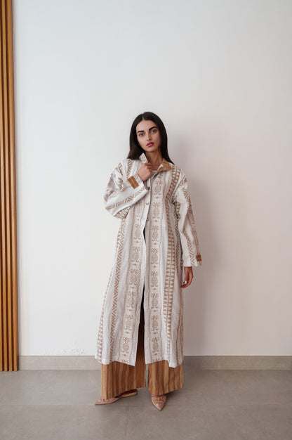 Woman wearing a long, patterned coat against a plain wall.
