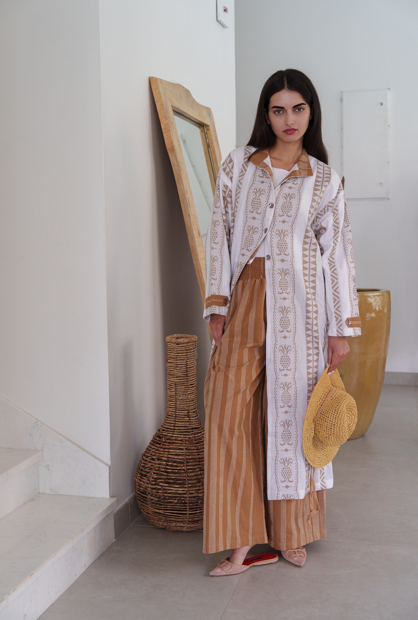 Woman in a stylish outfit standing in a minimalistic room with decorative vases.