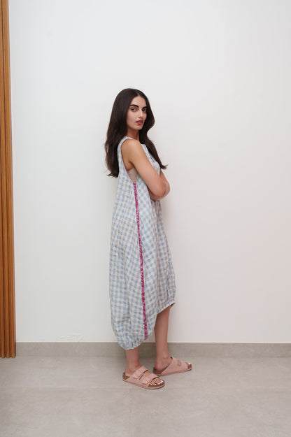 Woman wearing a checkered dress with a red border against a white wall.