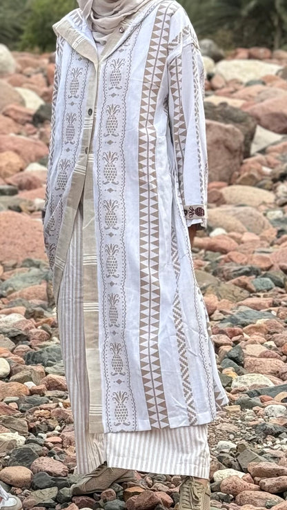 Person wearing a long, patterned dress standing on a rocky beach.