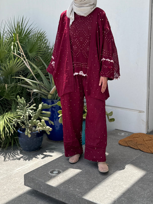 Handcrafted burgundy Bandhani set worn by model outdoors beside potted plants, artisanal Indian summer outfit